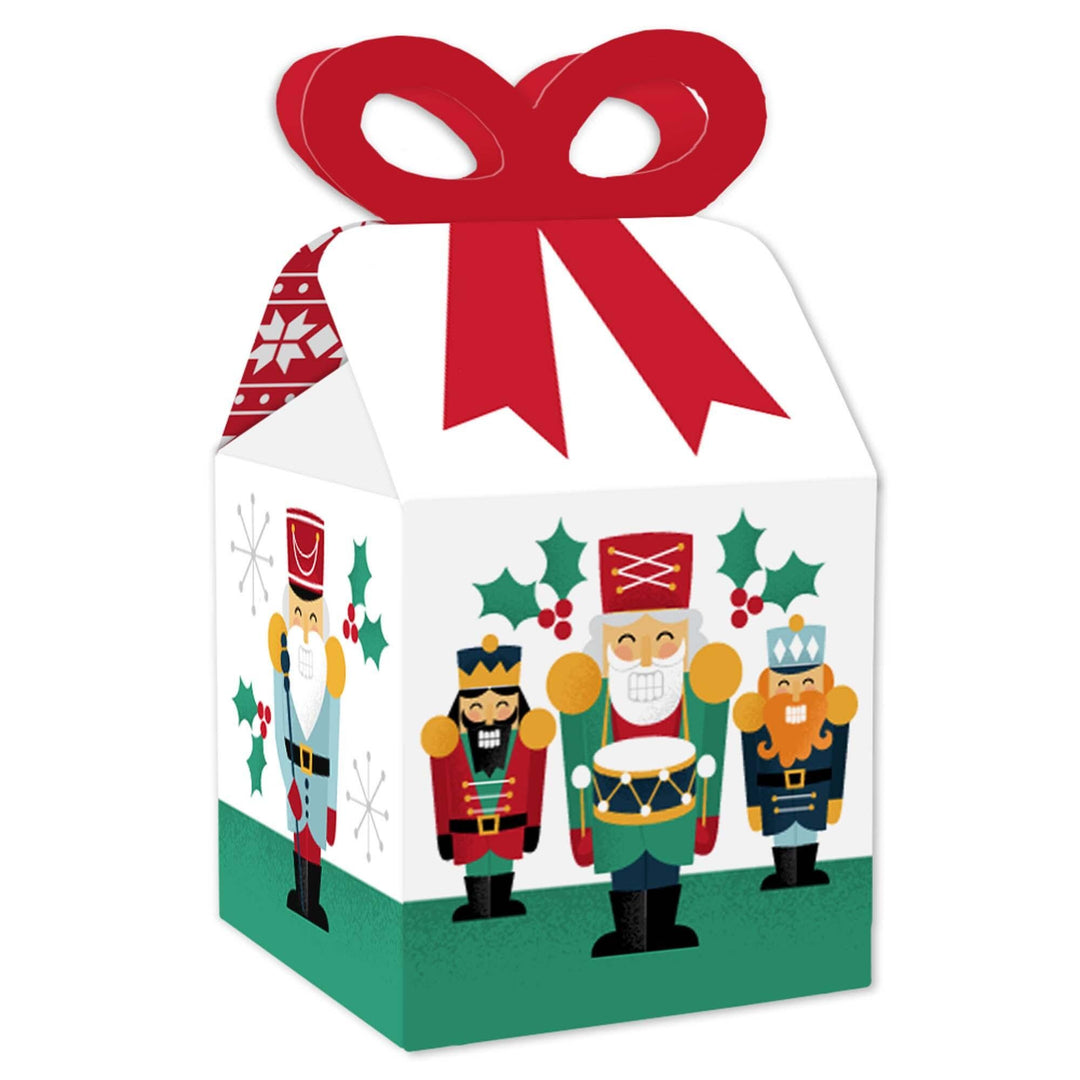 A square favor gift box with a Christmas Nutcracker theme, featuring colorful illustrations of nutcracker characters and holiday motifs, sealed with a red ribbon bow on top.