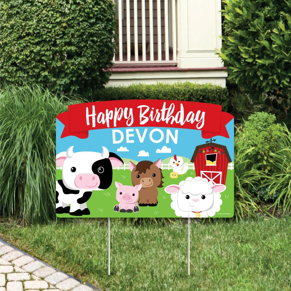 A colorful personalized Happy Birthday yard sign featuring farm animals like a cow, pig, and sheep with a red barn, displayed in a grassy outdoor area.