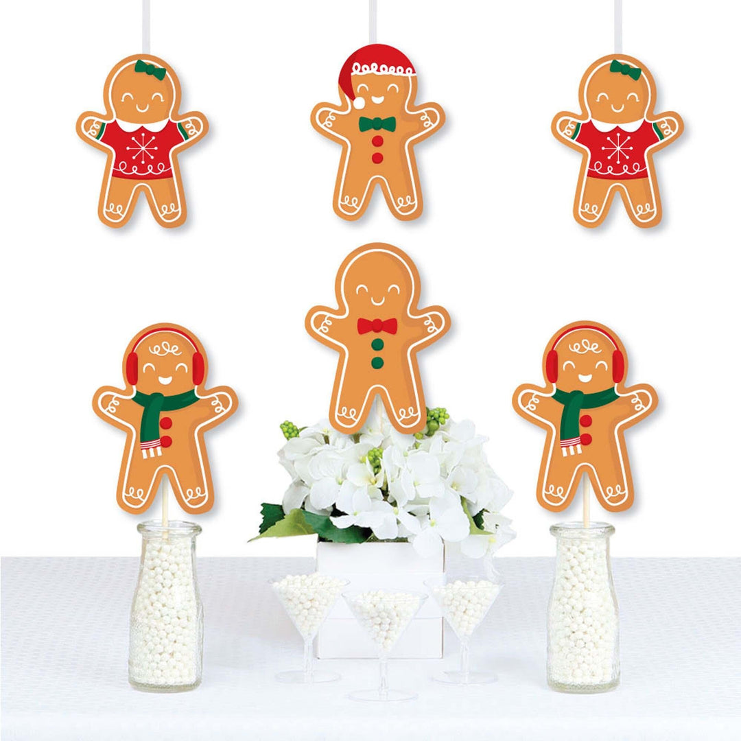 A set of die-cut gingerbread man shaped decorations printed on heavy card stock paper, displayed hanging from strings above a table decorated with white flowers and bottles.