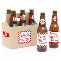 Six beer bottle labels with tropical flamingo design, attached to bottles in a kraft paper carrier, indicating the product is Christmas-themed.