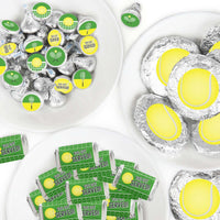 An arrangement of candy bars and candies decorated with green and yellow tennis ball-themed stickers, presented on white plates.