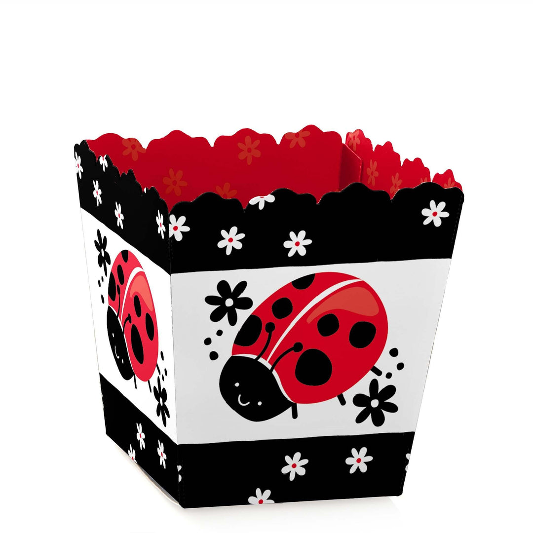 A small square party favor box with a white base and black borders, featuring a red ladybug and floral patterns, designed for a baby shower or birthday party.