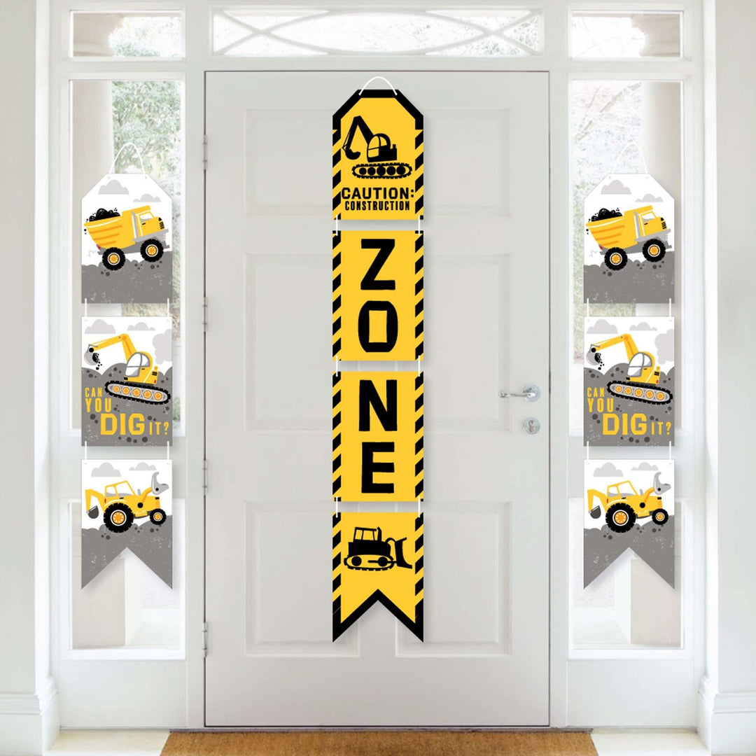 A set of vertical hanging paper banners with construction theme, including a 'ZONE' banner and others with construction vehicles and tools, displayed on a white door.
