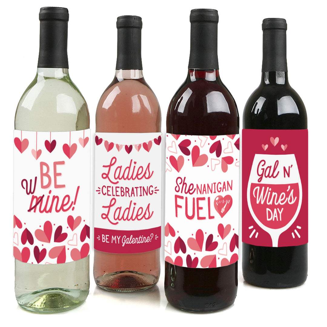Four wine bottles each with a different wine color and a unique sticker label with text and heart graphics. The stickers say 'BE mine', 'Ladies celebrating ladies', 'Shenanigans FUEL', and 'Gal n' Wine's DAY'.