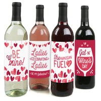 Four wine bottles each with a different wine color and a unique sticker label with text and heart graphics. The stickers say 'BE mine', 'Ladies celebrating ladies', 'Shenanigans FUEL', and 'Gal n' Wine's DAY'.